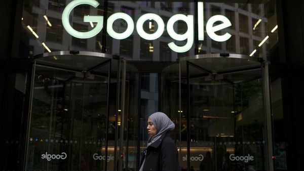 A woman walks past the front of a glass building with the Google logo.